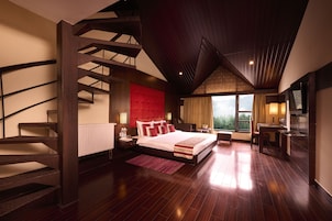 A modern bedroom with a large bed, a wooden staircase, a view of the outdoors, and a kitchen area.