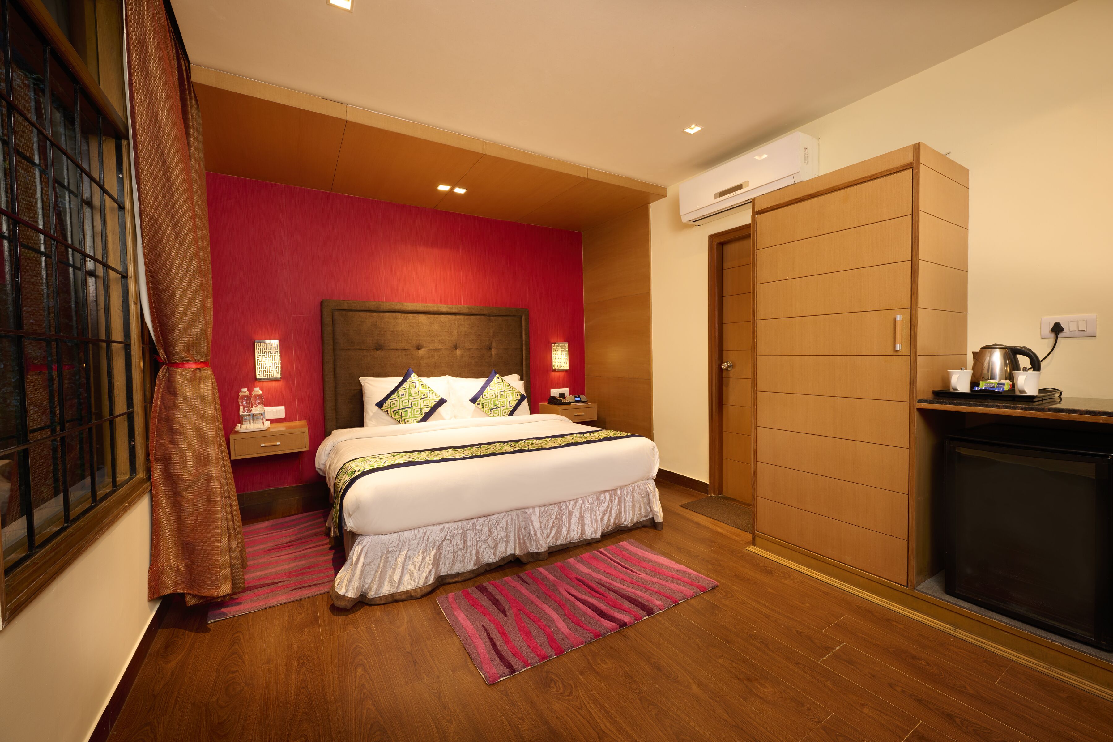 Ein Hotelzimmer mit einem großen Bett, einem Holzschrank, einer kleinen Küchenzeile und einem Fenster mit Vorhängen.