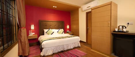 A hotel room with a large bed, a wooden wardrobe, a small kitchen area, and a window with curtains.