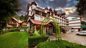 Un hotel de varios pisos con un estilo arquitectónico tradicional, que presenta un patio central con un área de estar cubierta y abundante vegetación.
