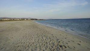 A wide sandy beach with footprints, calm water, and distant mountains. - Scala Apartments (Naxos)