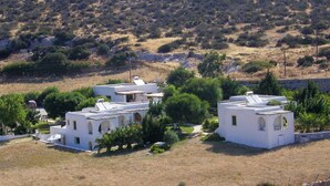 A cluster of white buildings with flat roofs, surrounded by greenery and a hilly landscape. - Scala Apartments (Naxos)