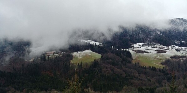 Un paysage montagneux avec des champs enneigés et un bâtiment niché au milieu des arbres.