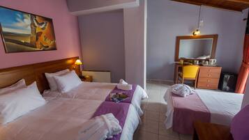 A hotel room with two beds, a wooden headboard, a painting, a desk with a chair, a mirror, and a small kitchenette.