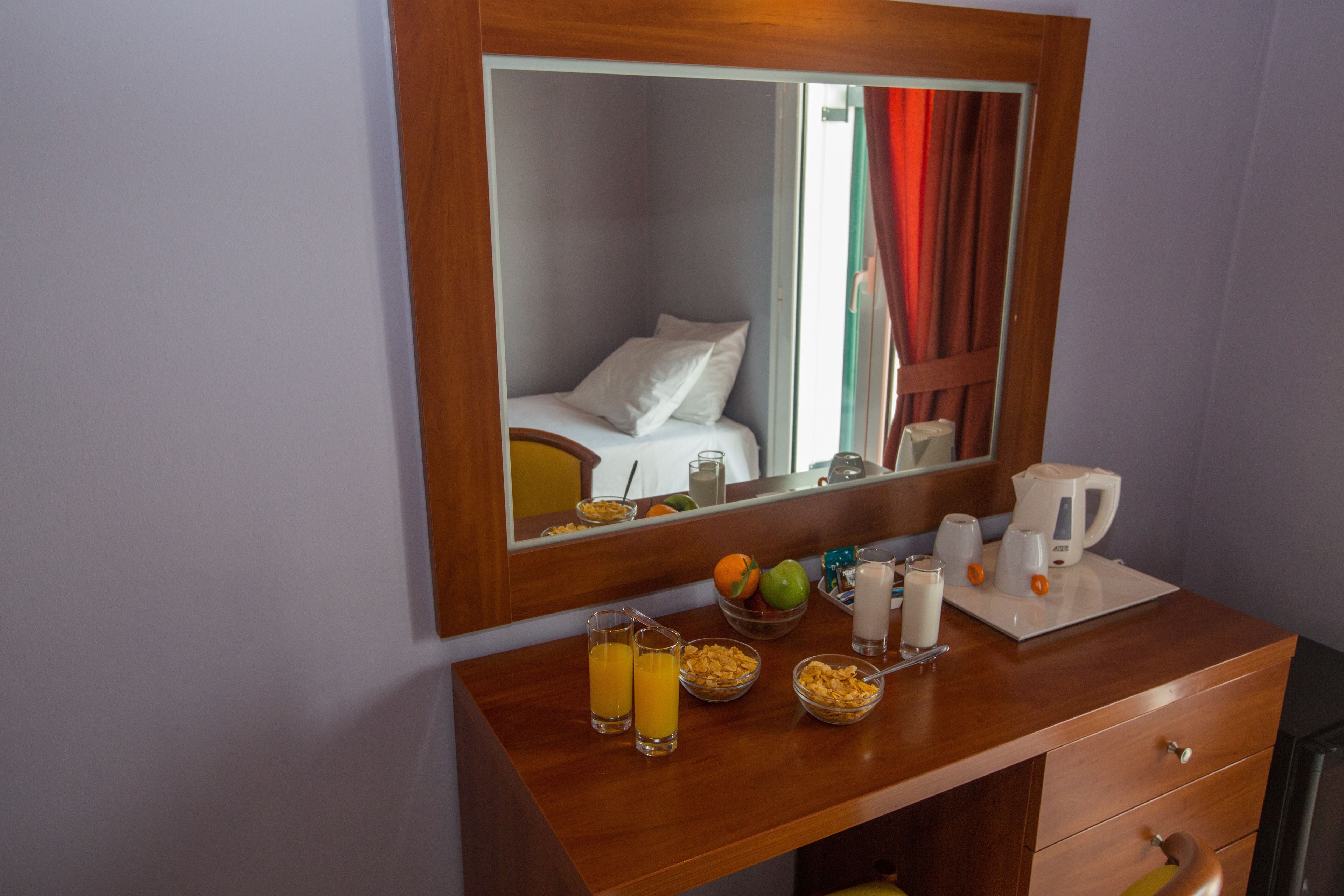 A hotel room with a wooden vanity, a bed with white linens, a mirror, and breakfast items including cereal, orange juice, and coffee.