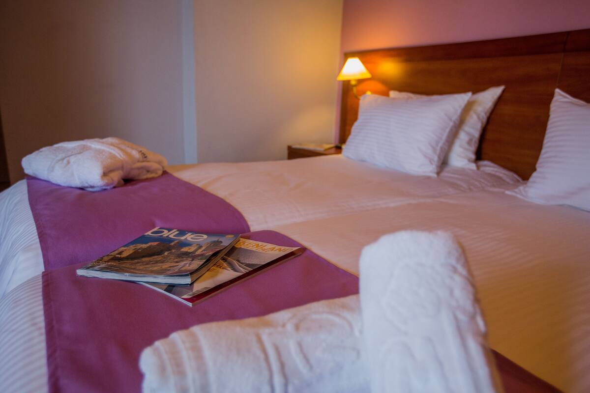 A neatly made bed with white linens, a purple throw blanket, and a magazine on the pillow.