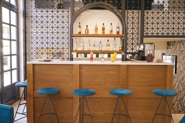 A bar area with wooden stools, a shelf with various bottles, and a patterned wall. - Mirabel Hotel (Kefalonia)
