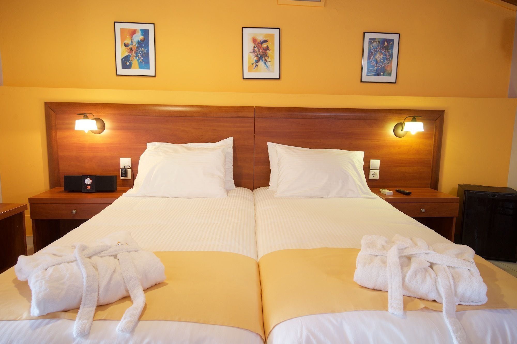 A double bed with two white pillows, a wooden headboard, bedside tables with lamps, and three framed artworks on the wall.