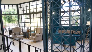 Una habitación con un ventanal grande, un sofá, dos sillones y una mesita con una lámpara.