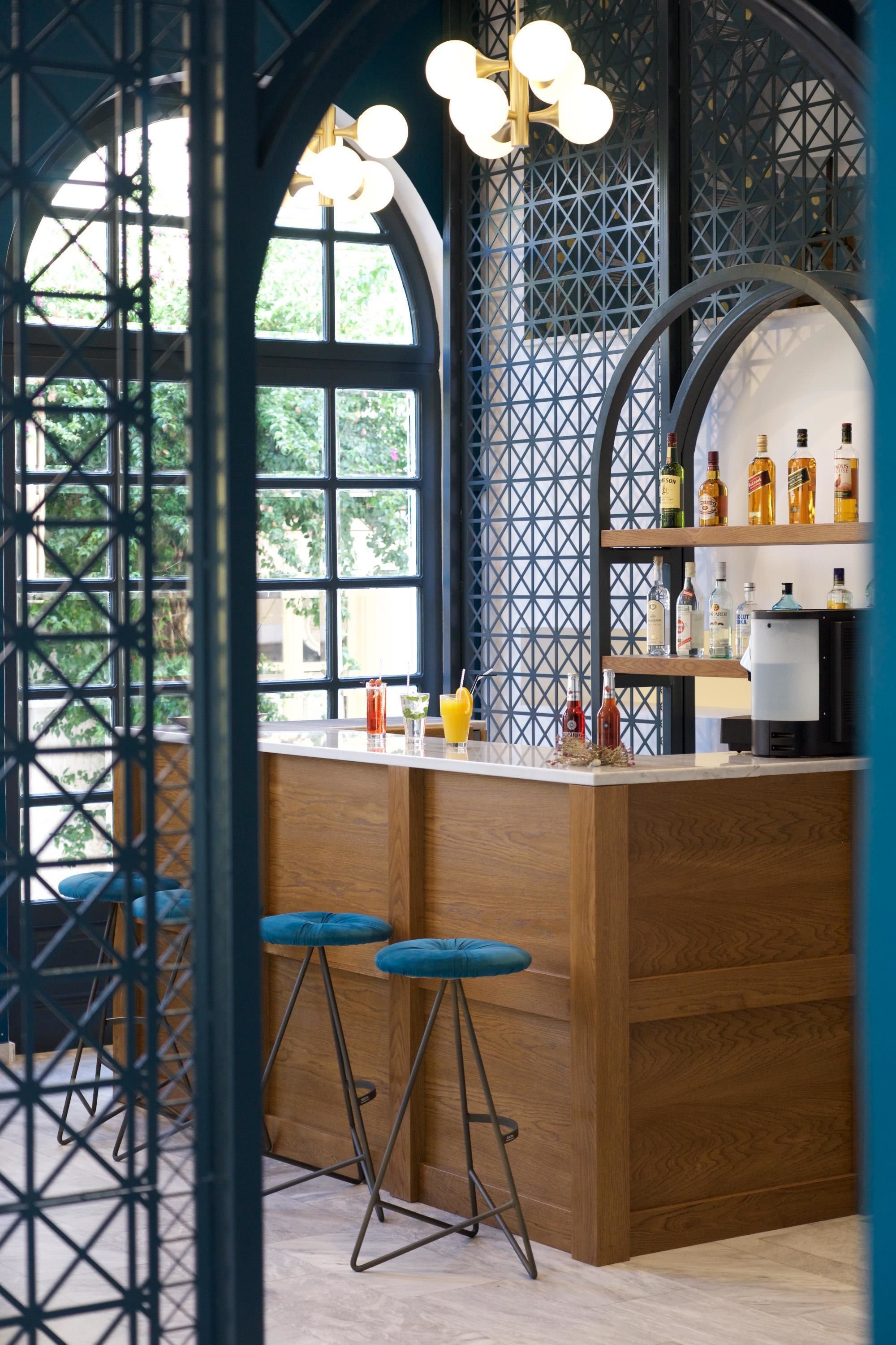 Zona de bar con taburetes de madera, una barra y estantes con botellas.