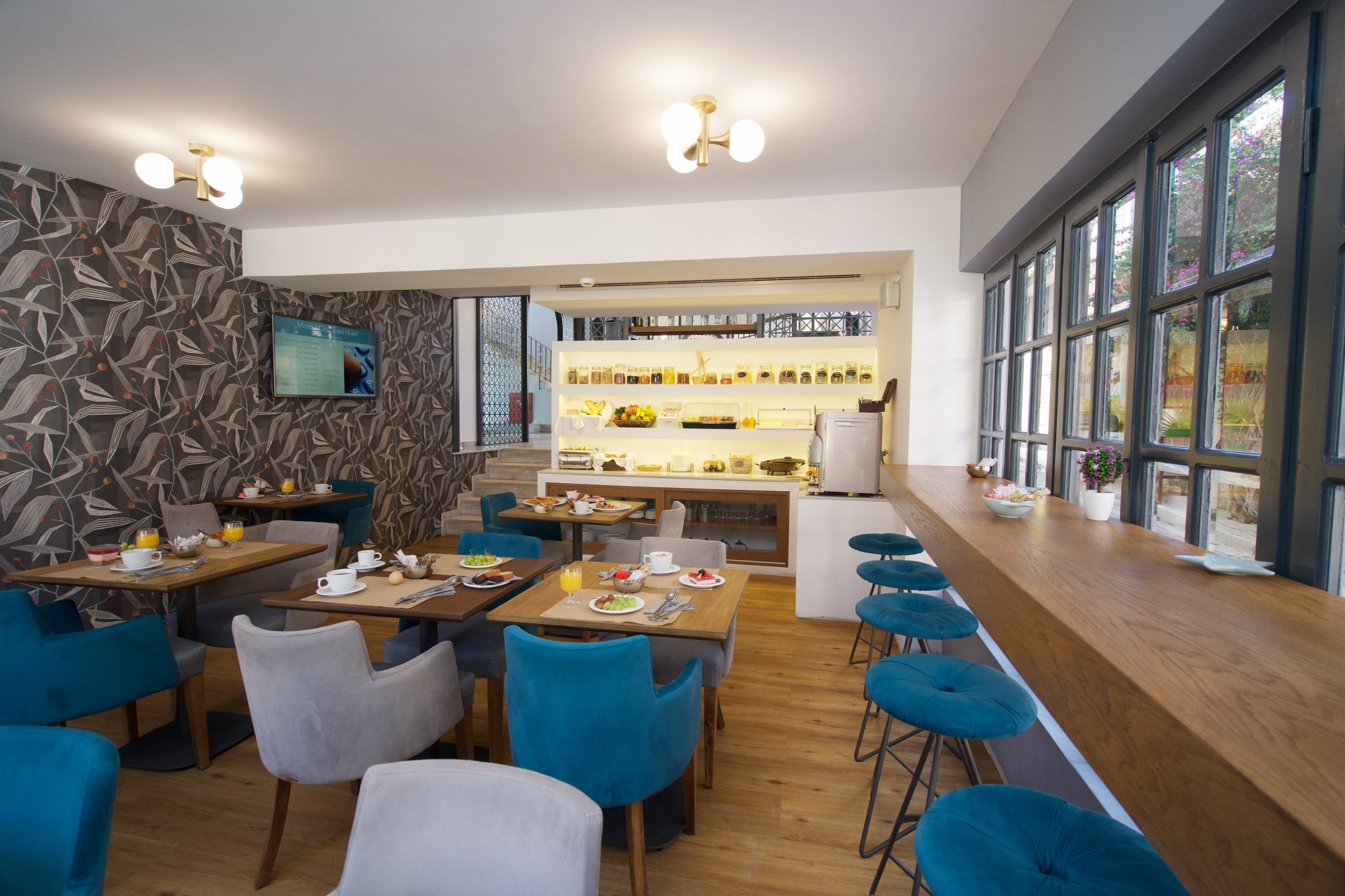 Ein modernes Restaurant mit Holztischen und blauen Stühlen, ein Barbereich mit Hockern und eine Küche im Hintergrund.