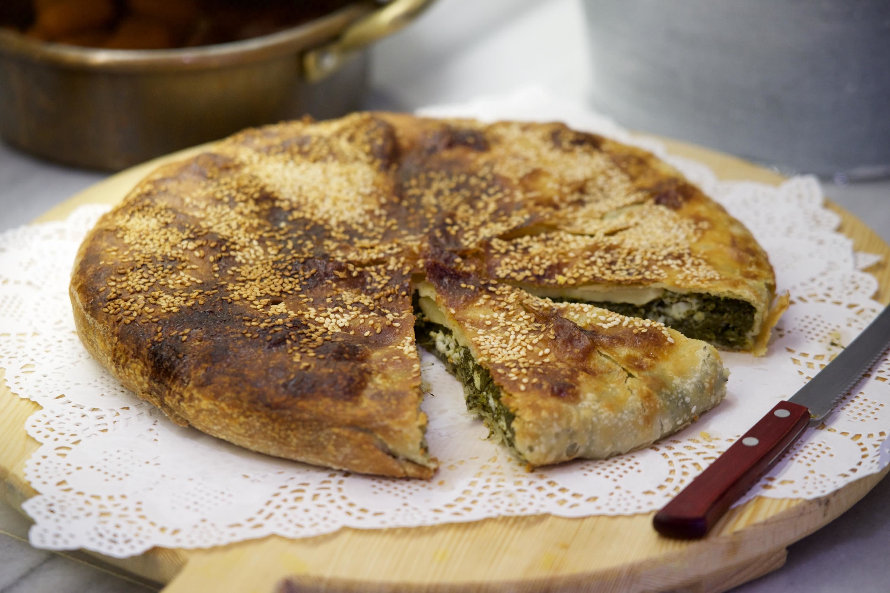 A round, sesame-seed-topped pastry on a wooden board with a knife beside it.