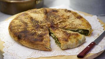 A round, sesame-seed-topped pastry on a wooden board with a knife beside it.