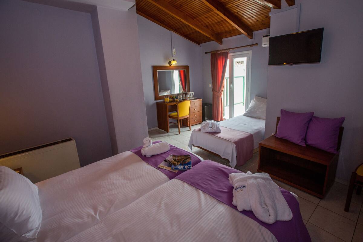 A hotel room with two beds, a desk with a chair, a TV, and a window with curtains.