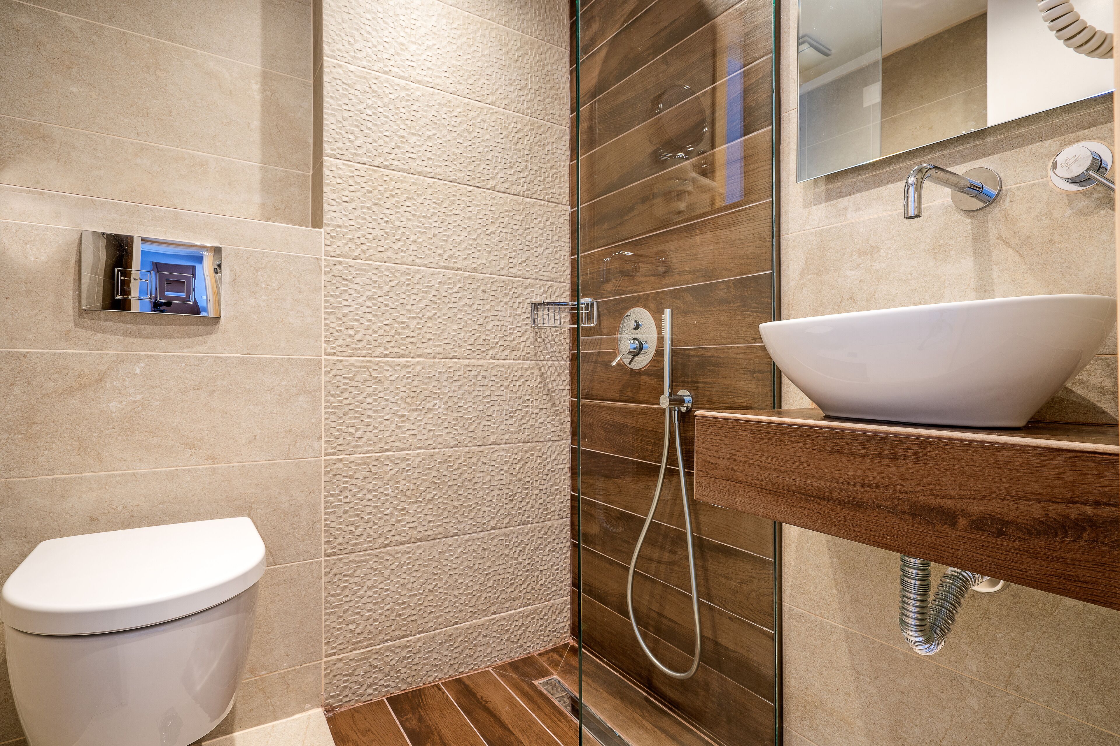 Een moderne badkamer met toilet, een douche met glazen wanden en een wastafel met een houten plankje.