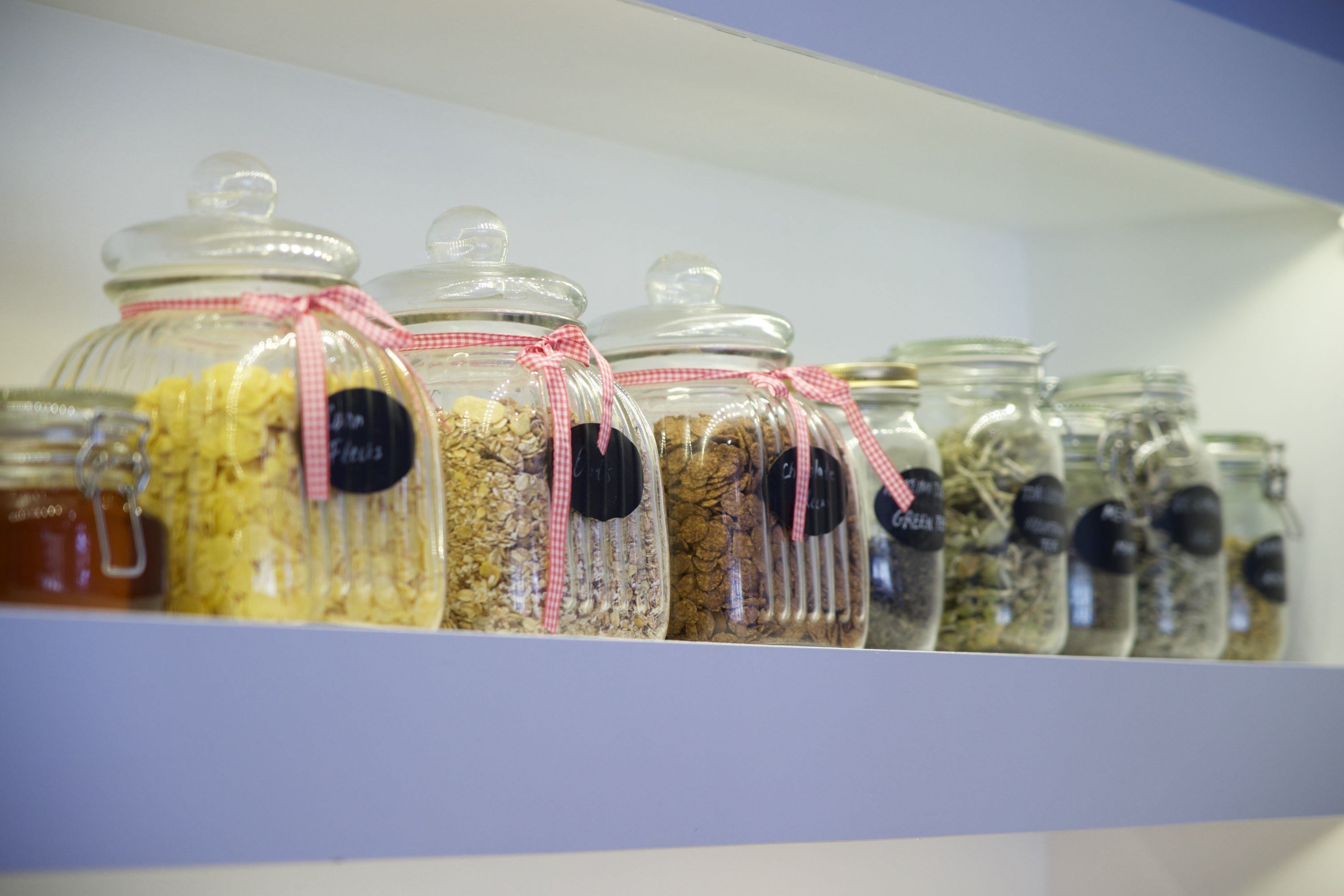 Una estantería con varios frascos de vidrio que contienen diferentes alimentos, cada uno sujeto con un lazo de cuadros.