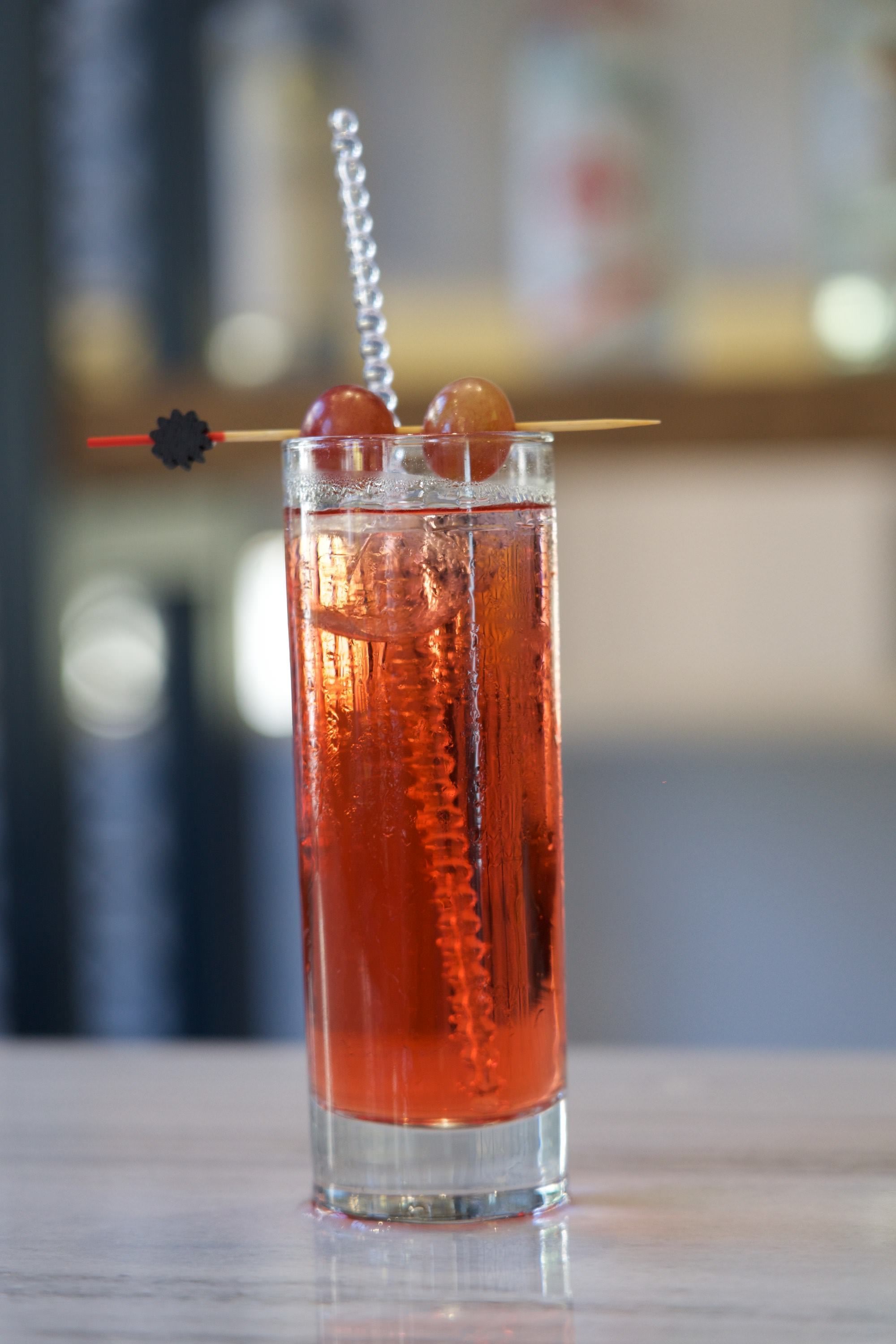 A tall glass with a red beverage, ice cubes, and a straw with a decorative element.