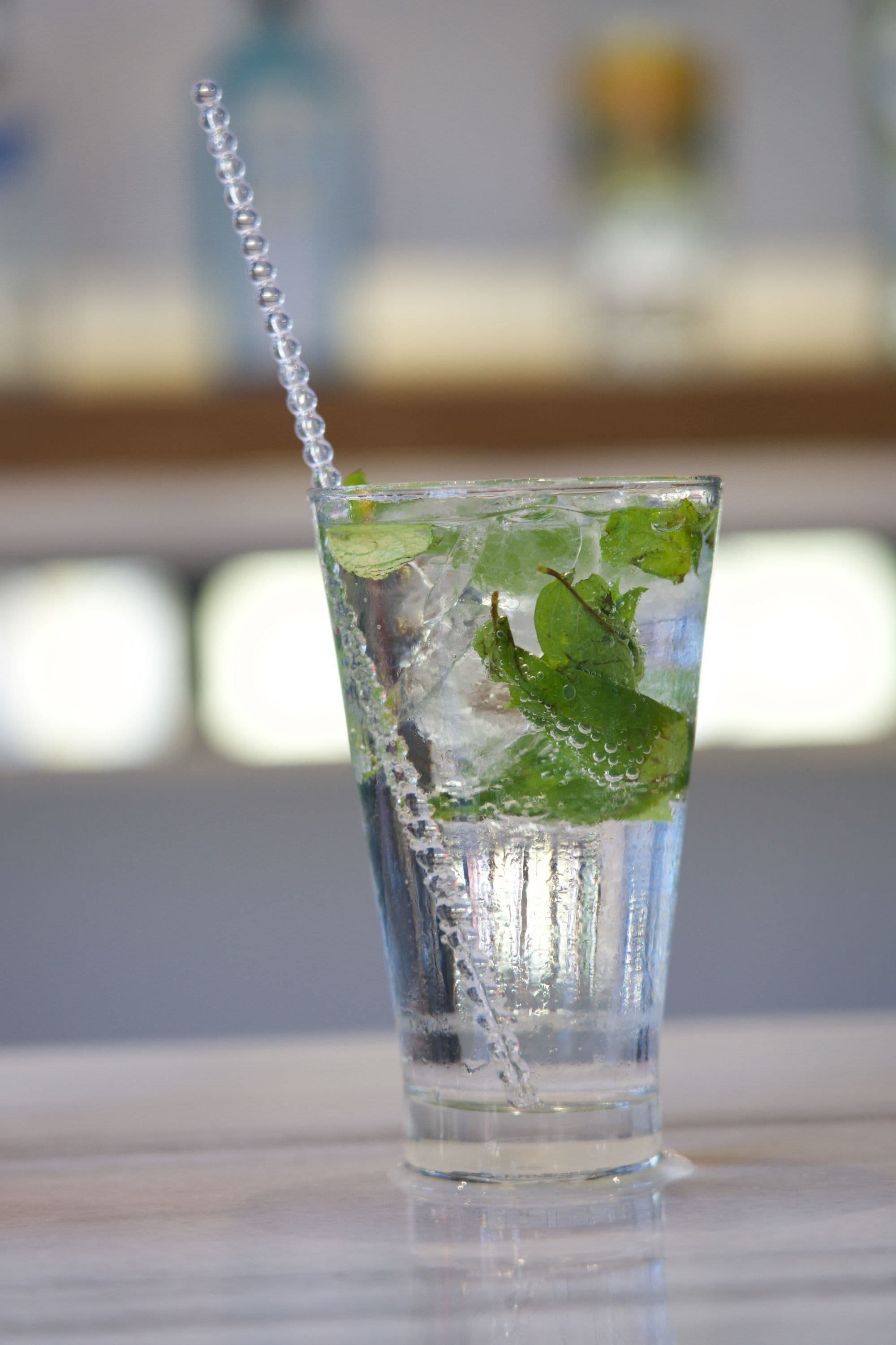 A tall glass with ice cubes and mint leaves, with a clear liquid and a straw.
