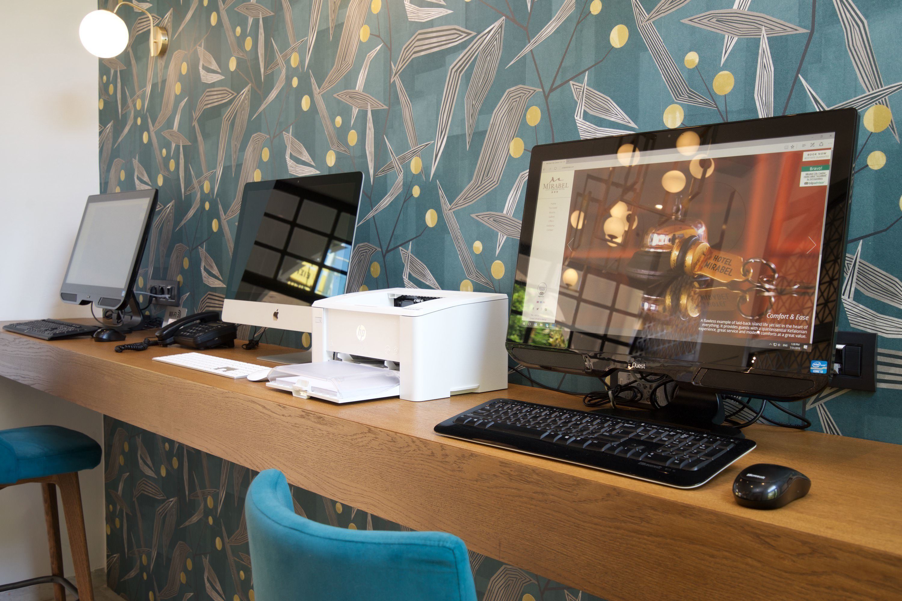 A hotel reception desk with a desktop computer, a printer, and a keyboard.