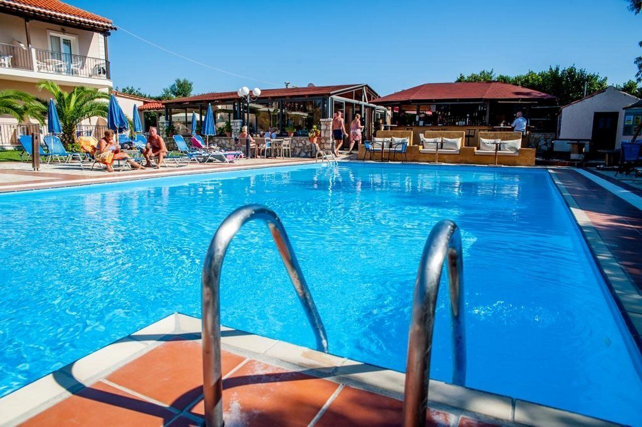 A swimming pool with lounge chairs and umbrellas, a bar area, and a building with balconies.