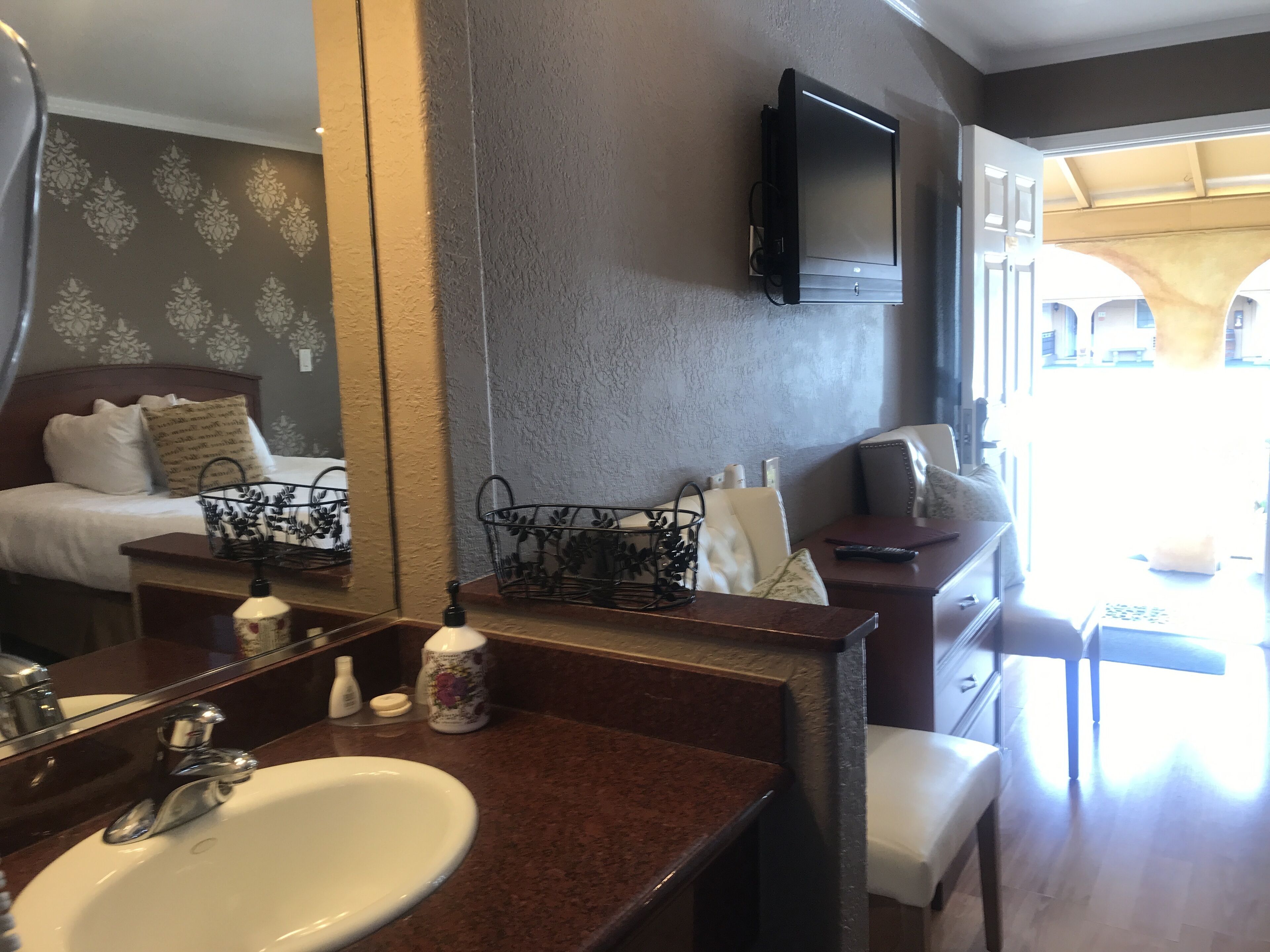 A hotel room with a large mirror, a bed with a headboard, a sofa, a small table, and a TV mounted on the wall.