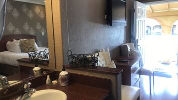 A hotel room with a large mirror, a bed with a headboard, a sofa, a small table, and a TV mounted on the wall.