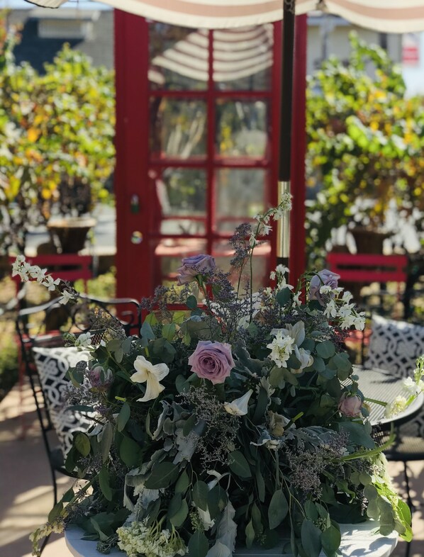 A table with a floral centerpiece, a red door, and outdoor seating.