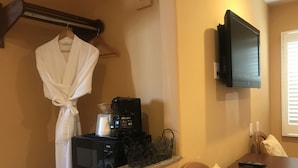 A hotel room with a kitchenette, a TV mounted on the wall, a robe hanging on a hook, and a bed with a pillow. - Chardonnay Lodge (Napa)