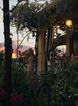 A garden with a statue, a pergola with vines, and a sunset in the background.