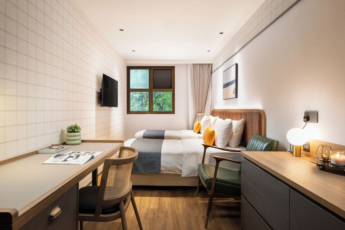 A modern hotel room with a bed, desk, chair, and a TV mounted on the wall.