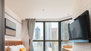 A modern hotel room with a large window, a flat-screen TV mounted on the wall, and a bed with a headboard. - Dash Living On Hollywood (Hong Kong)