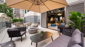 An outdoor seating area with a large umbrella, wicker chairs, a round table, and a sofa. - Dash Living On Hollywood (Hong Kong)