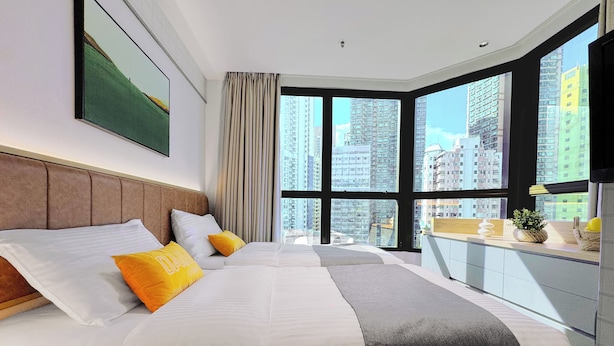 A modern hotel room with a large bed, a view of tall buildings, and a balcony with a view. - Dash Living On Hollywood (Hong Kong)