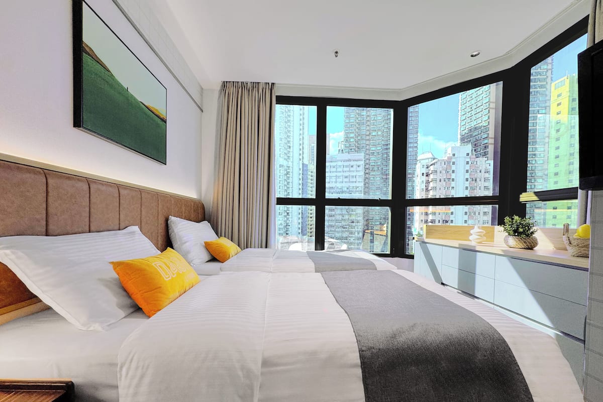 A modern hotel room with a large bed, a view of tall buildings, and a balcony with a view.