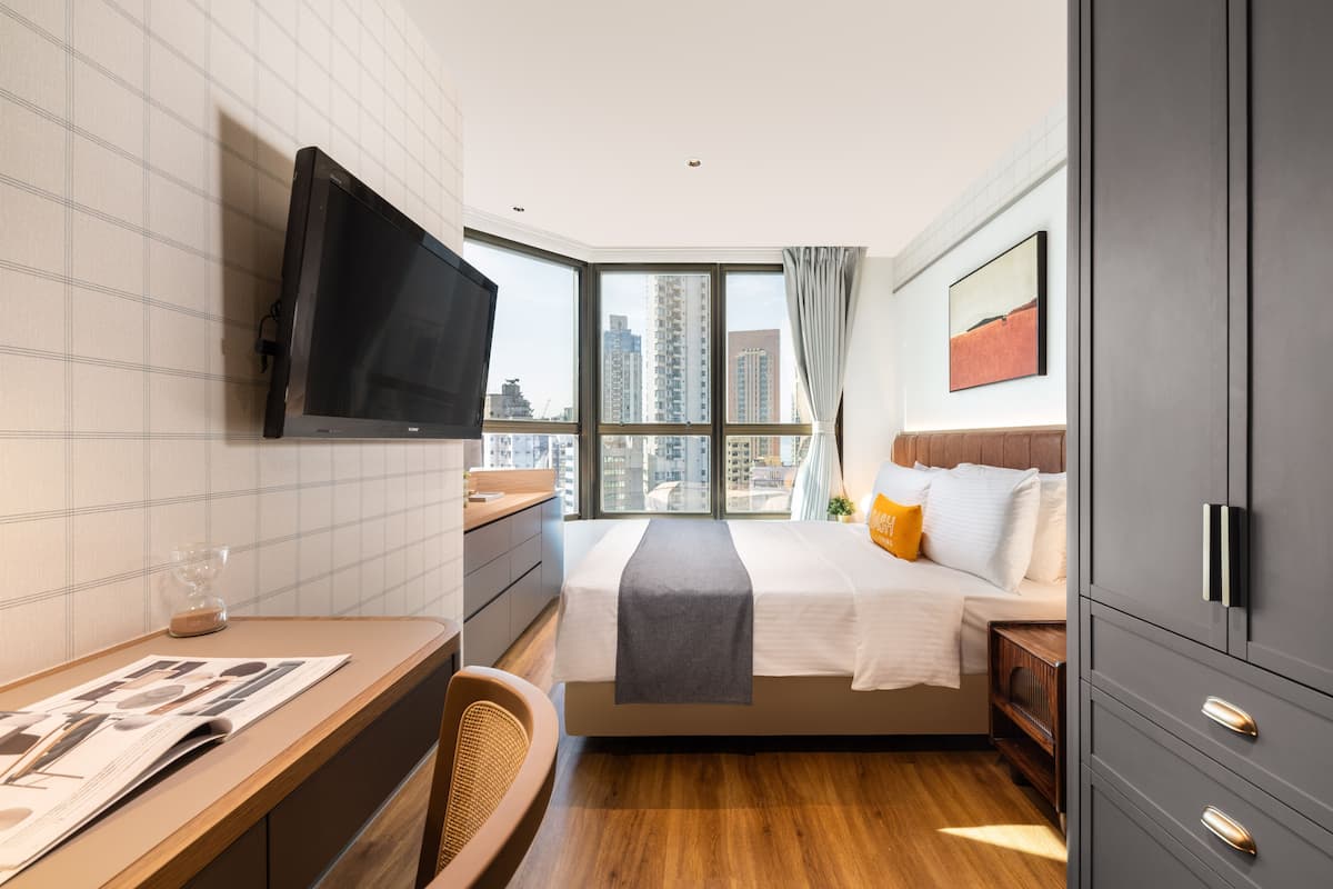 A hotel room with a large bed, a desk, a television, and a view of the city.