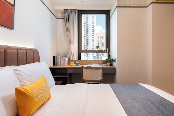 Habitación de hotel con cama, escritorio, silla y ventana con vista a edificios altos, además de una cortina.