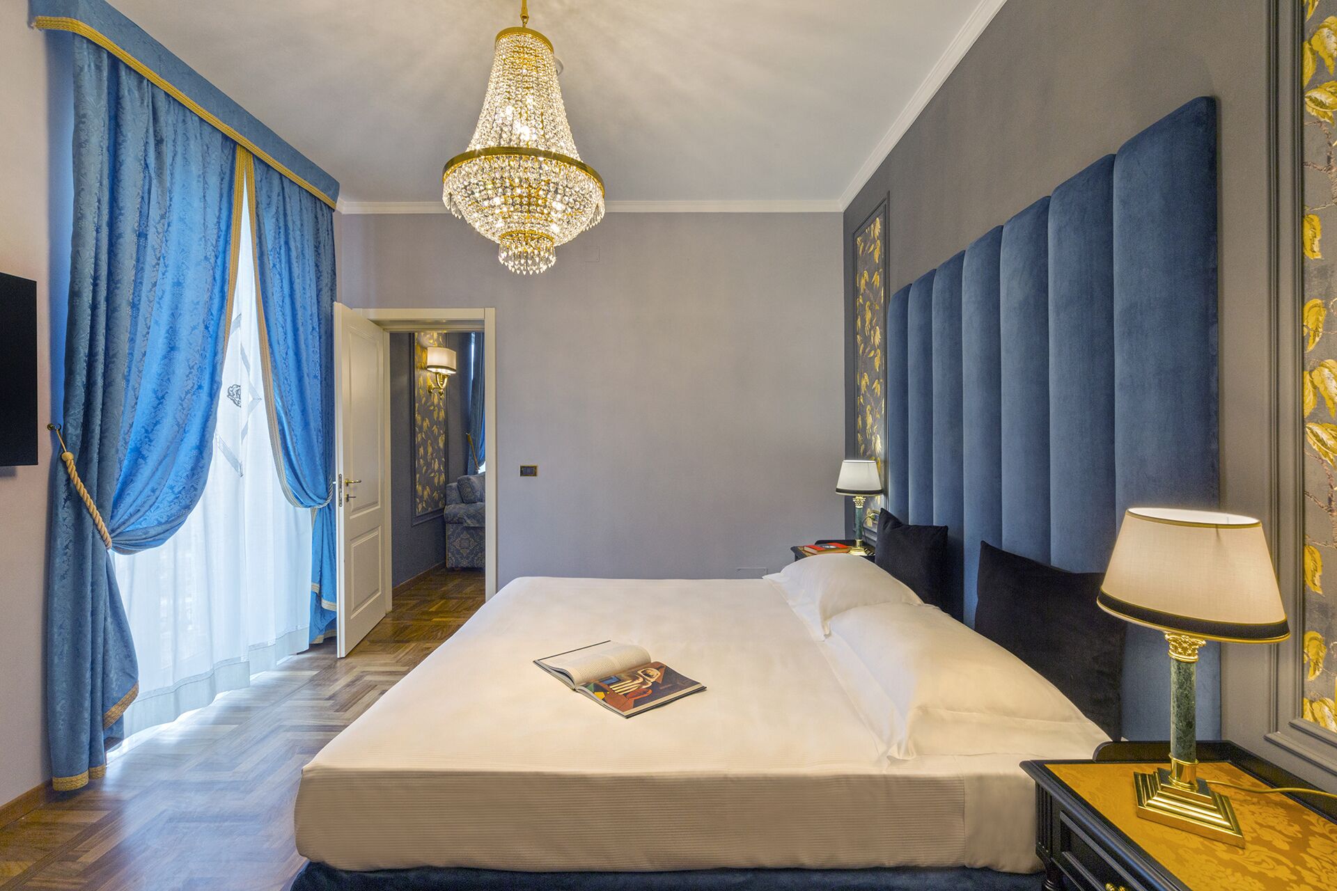 Une chambre d’hôtel avec un grand lit, un lustre et une vue sur un couloir.