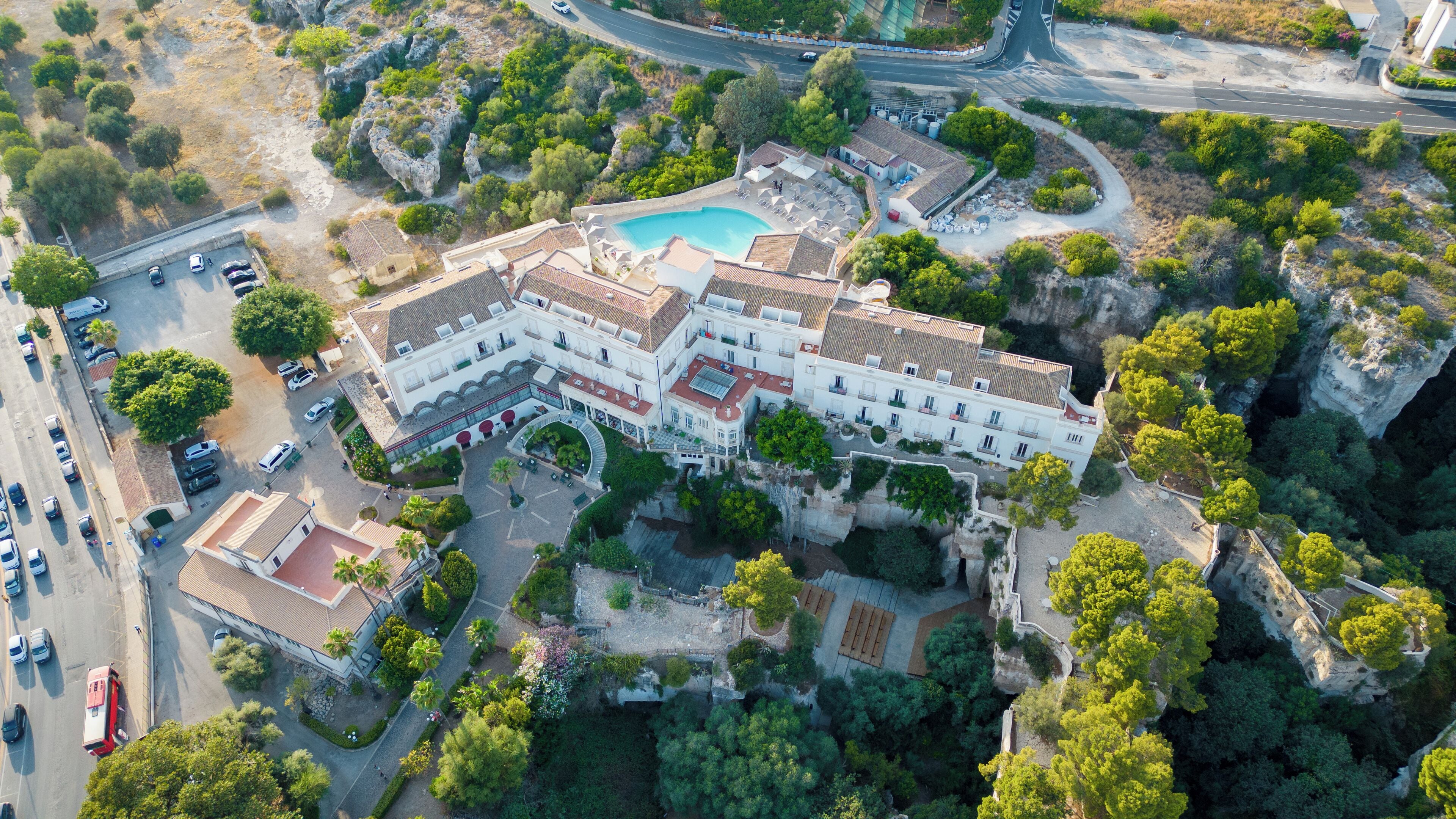 Vista aérea de um hotel com piscina, cercado por vegetação e terreno rochoso.