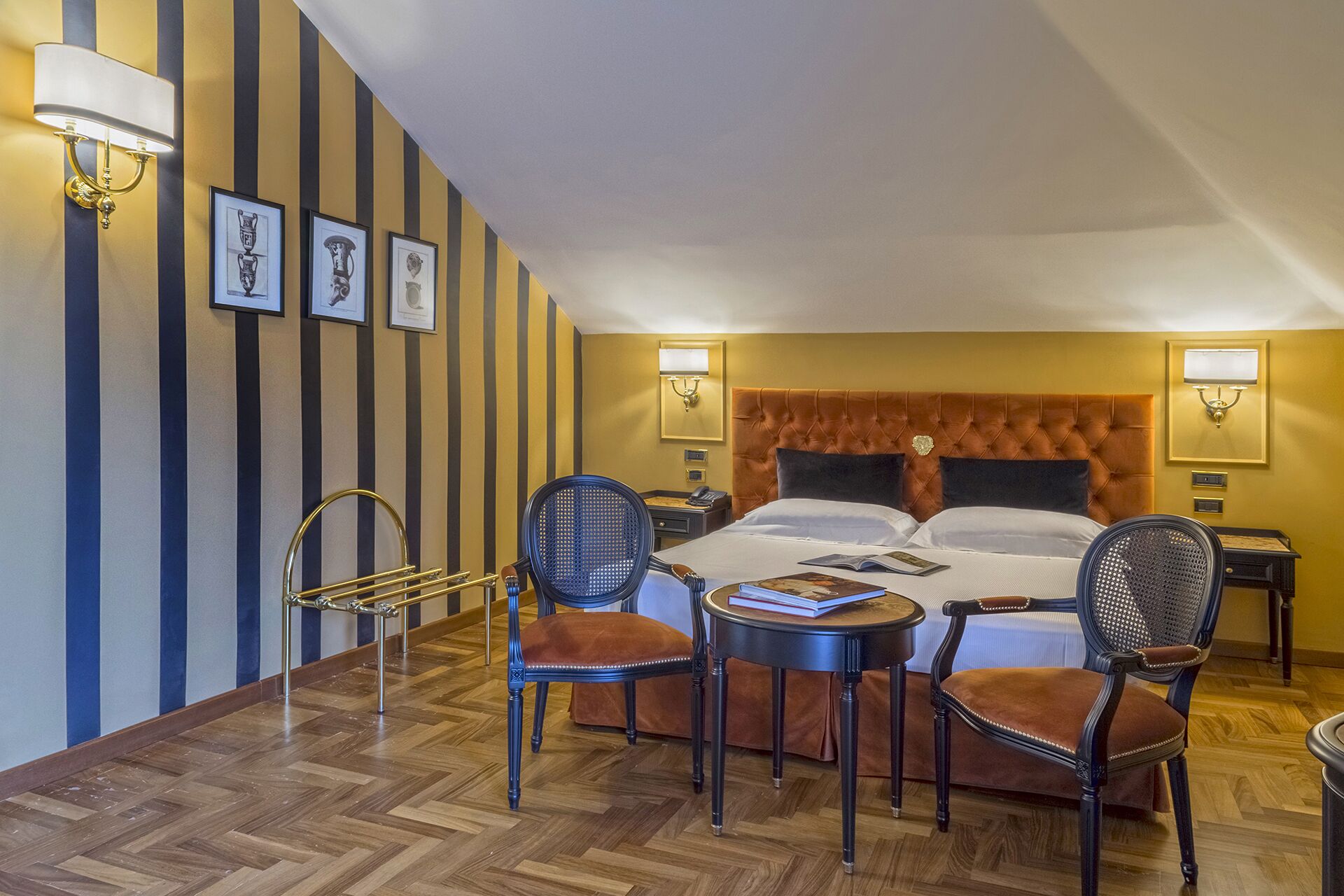A hotel room with a large bed, two bedside tables, a chair, a small table, and a wall-mounted lamp.