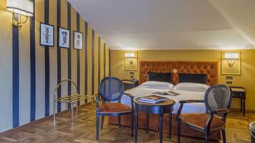 A hotel room with a large bed, two bedside tables, a chair, a small table, and a wall-mounted lamp.