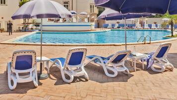 A poolside area with lounge chairs and umbrellas, a swimming pool, and a building in the background.