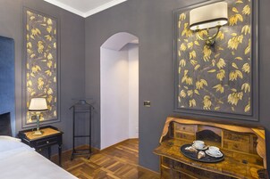A hotel room with a bed, a nightstand with a lamp, a wooden side table with a tray of pastries, and a wall-mounted light fixture.