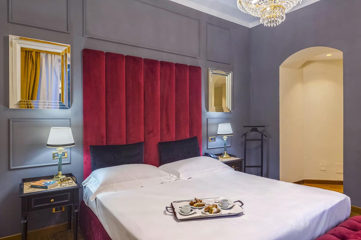 A hotel room with a large bed, red curtains, a chandelier, and a tray with pastries.