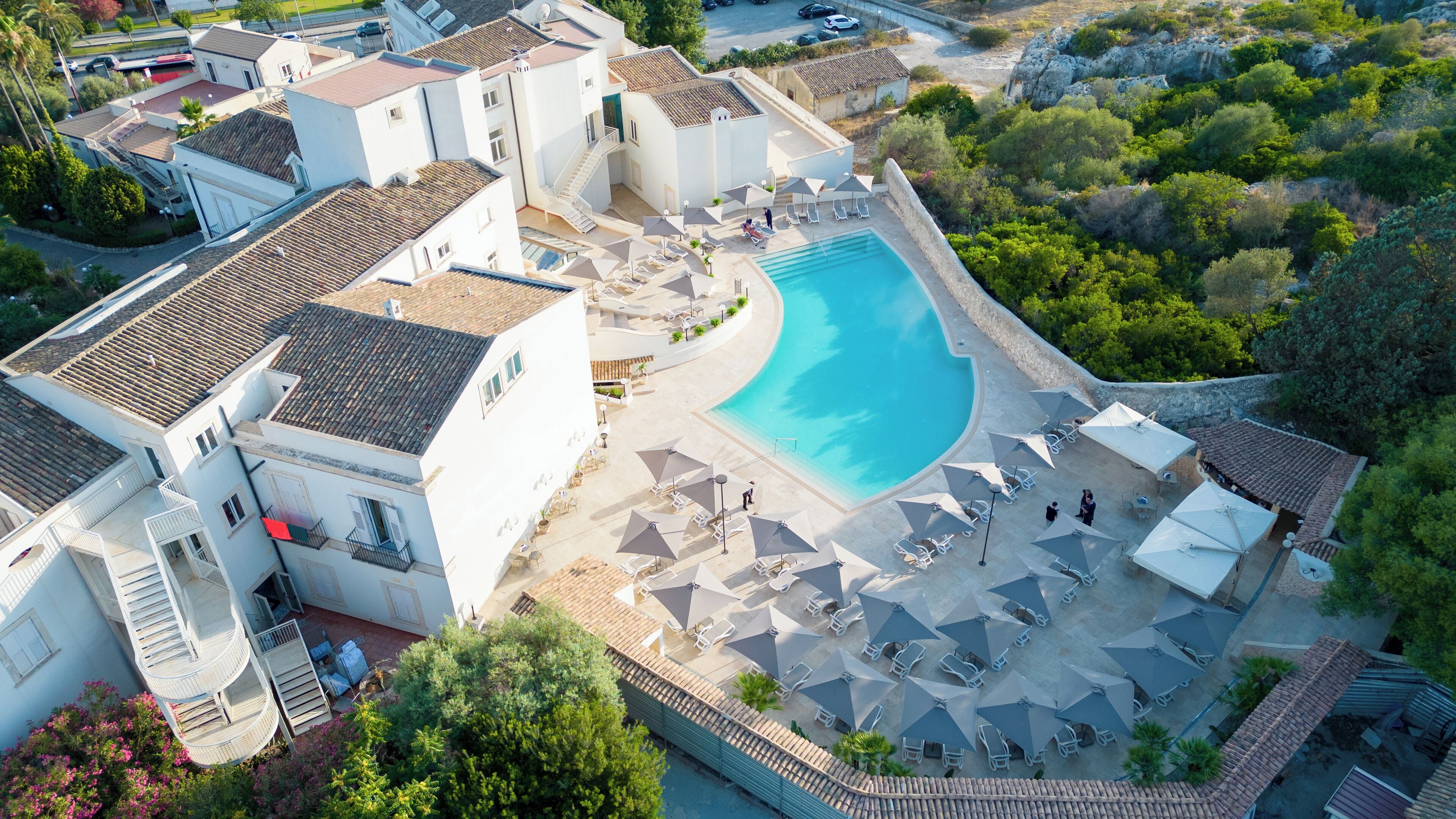 An aerial view of a resort with a swimming pool, multiple buildings, and outdoor seating areas.
