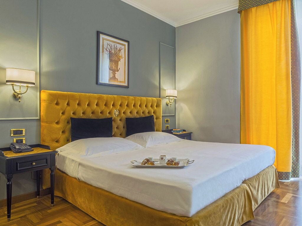A hotel room with a large bed, two bedside tables, a nightstand, a framed picture on the wall, and a yellow curtain.