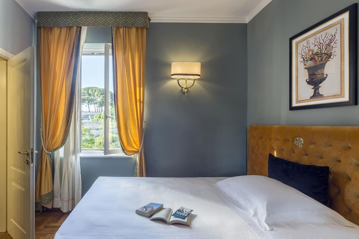 A neatly made bed with two books, a wall-mounted lamp, and a framed artwork above it.