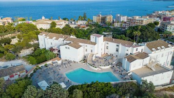 A coastal hotel with a swimming pool, multiple balconies, and a view of the sea.