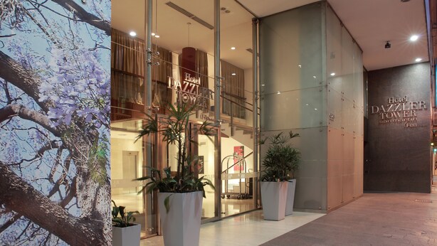 A modern hotel entrance with glass doors, indoor plants, and a visible interior including a staircase.