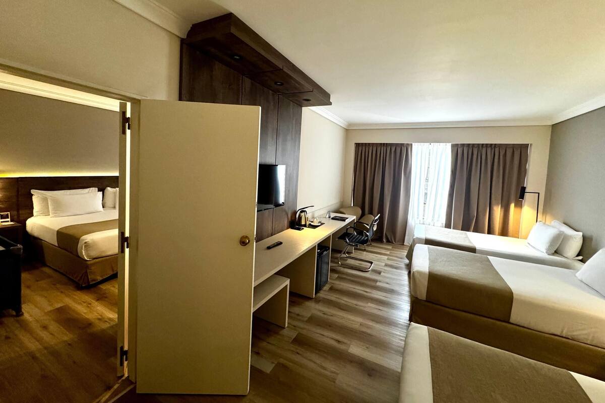 A hotel room with a bed, a desk with a chair, a sofa, a TV, and a window with curtains.