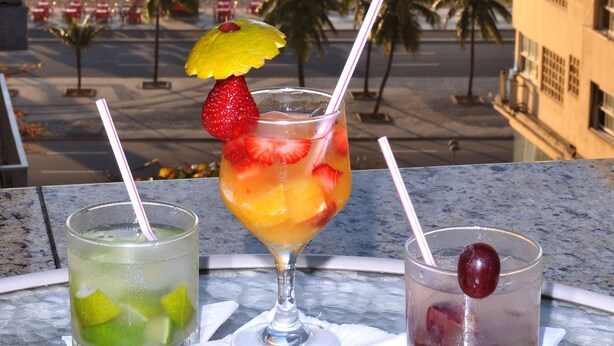 Two cocktails on a table with a view of the beach and palm trees. - Windsor Martinique Copacabana (Rio de Janeiro)